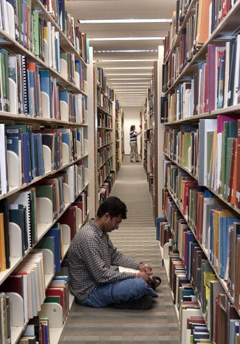Photo of Founders Memorial Library patron reading between the shelves.