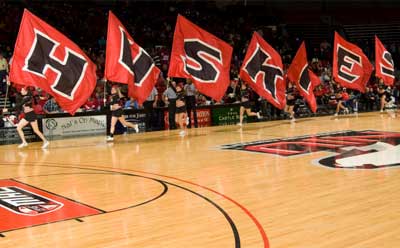 NIU cheerleaders run basketball court with H-U-S-K-I-E-S flags