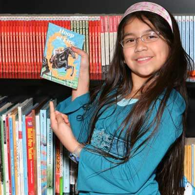 Photo of a young girl in a library pointing to a book