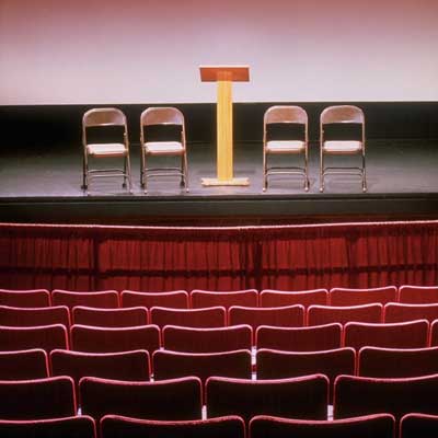 Photo of an auditorium with four chairs and a lectern on the stage