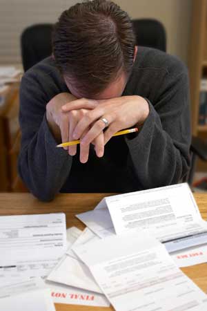 Photo of a man hanging his head over a pile of unpaid bills