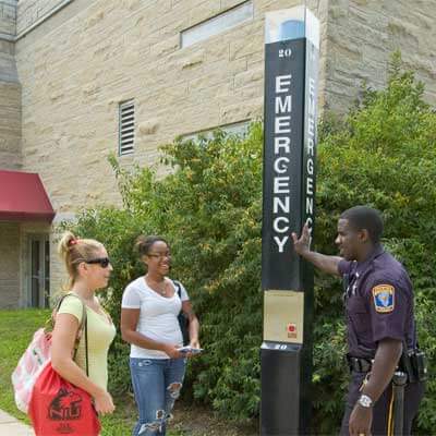 An NIU police officer speaks with students next to an emergency call box.