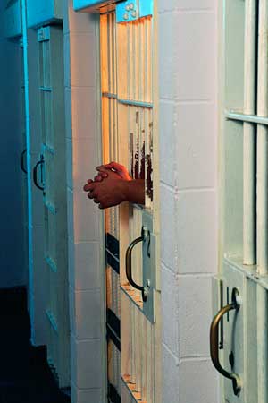 Photo of folded hands inside a jail cell door