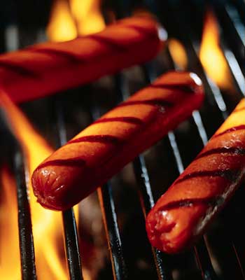 Photo of three hot dogs on a flaming grill