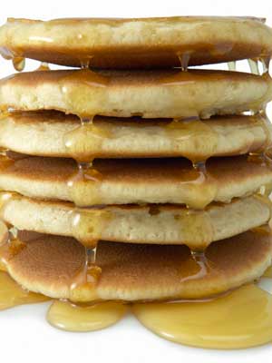 Photo of a stack of pancakes dripping in syrup