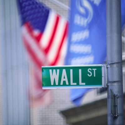 Photo of a Wall Street street sign with a U.S. flag in the background
