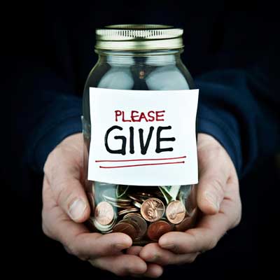 Photo of hands holding a glass jar of coins with a "Please Give" label