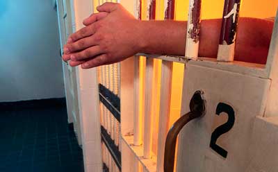 Photo of hands and arms reaching through prison cell bars
