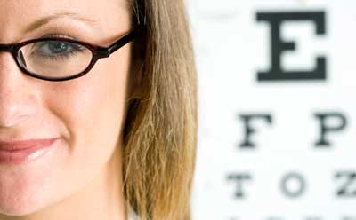 Photo of a woman in glasses next to a eye chart