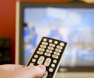 Photo of a hand pointing a remote control toward a TV