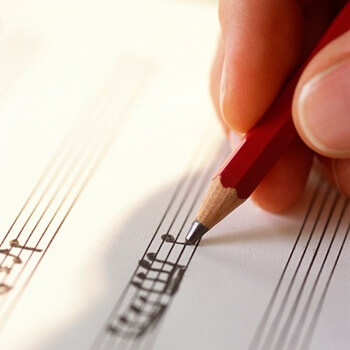 Photo of a hand and pencil writing musical notes on a staff