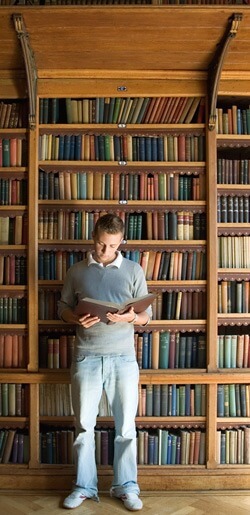 Photo of a man reading a book in front of a library shelf