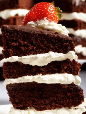 Photo of layered chocolate cake with white frosting and a strawberry on top