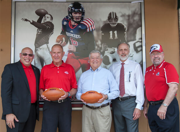 For the second consecutive fall, NIU and the City of DeKalb have partnered to display window clings at DeKalb businesses featuring the NIU football program. From left: NIU Associate Vice President/Director of Athletics Sean Frazier, Huskie football legends George Bork and Bob Heimerdinger, NIU President Doug Baker and DeKalb Mayor John Rey unveil the first of the new clings July 22 at the Lincoln Inn in downtown DeKalb. 