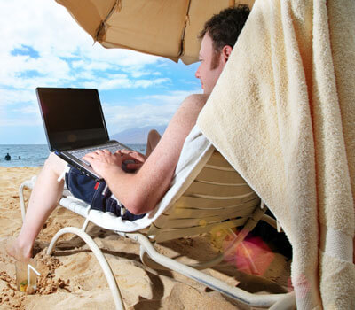 Photo of a man working on a laptop computer while at the beach